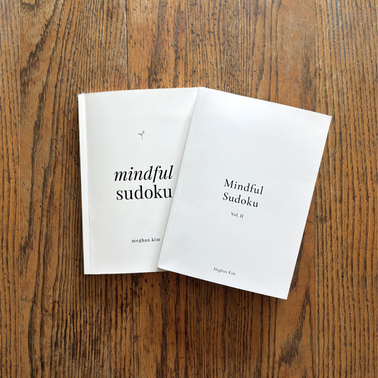 The Mindful Sudoku Original journal and Volume II paperbacks side by side on a wooden table